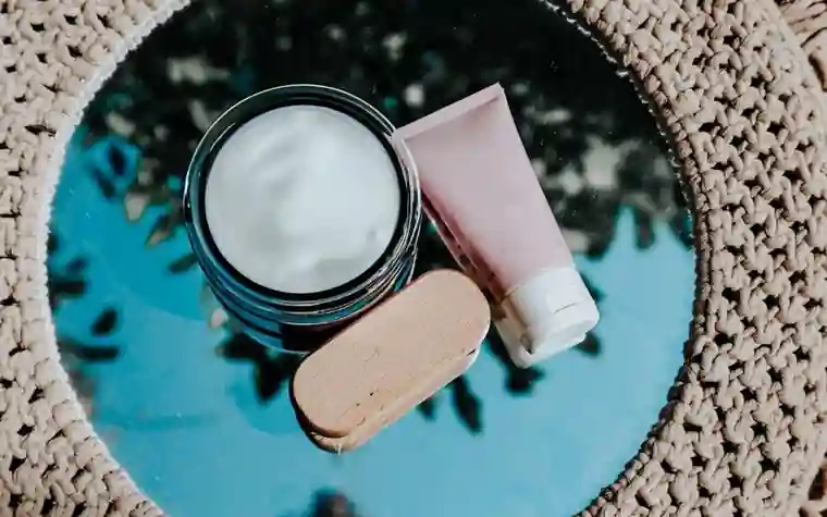 Open jar of moisturizer cream next to a tube on a reflective surface