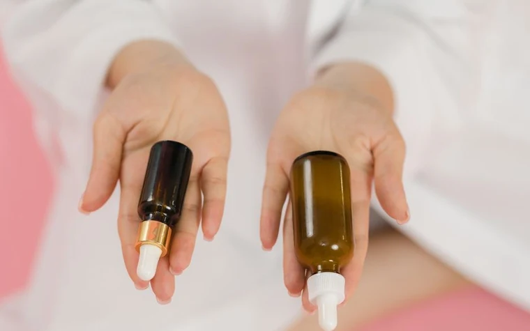 Hands holding two amber glass dropper bottles