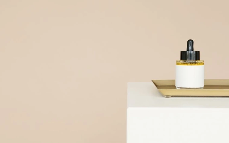 A dropper bottle of serum standing on a pale surface