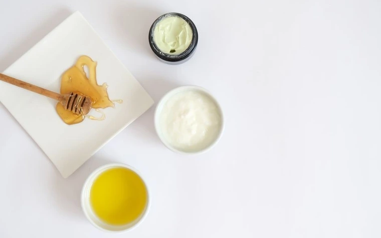 Flat lay of honey, moisturizing cream, and a small bottle of oil arranged on a white surface