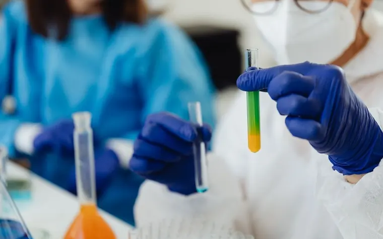 Two researchers in blue gloves and lab coats examining color-changing liquid in test tubes