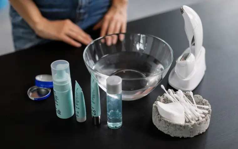 Overhead flat lay of skincare bottles, a glass bowl, and cotton pads on a dark surface