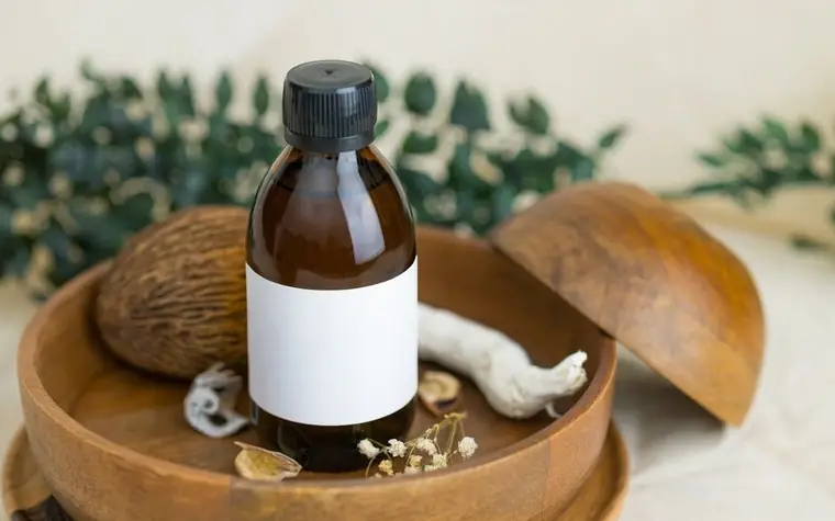 Amber dropper bottle with a blank label resting in a wooden bowl among dried plants