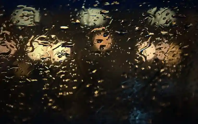 Raindrops on window glass with soft blurred lights behind
