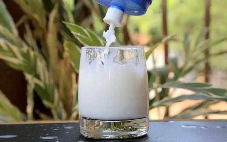 White milk poured into a glass tumbler with a plant behind it