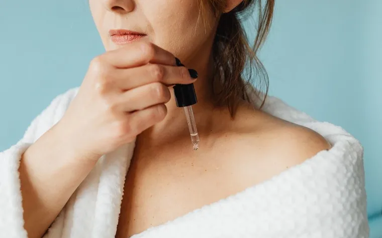 A woman applying serum with a dropper to her jawline after a shower