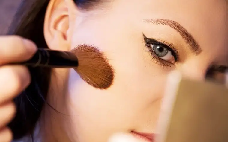A makeup brush sweeping cream-colored product across a cheek
