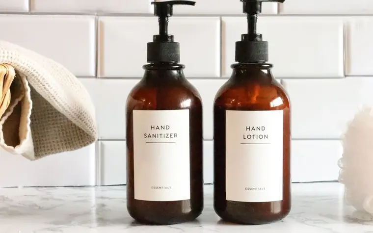 Two amber glass pump bottles with plain white labels standing on a white tiled counter