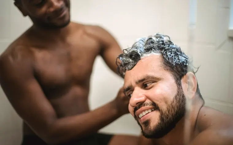 Man lathering shampoo foam through his hair while smiling in a bathroom