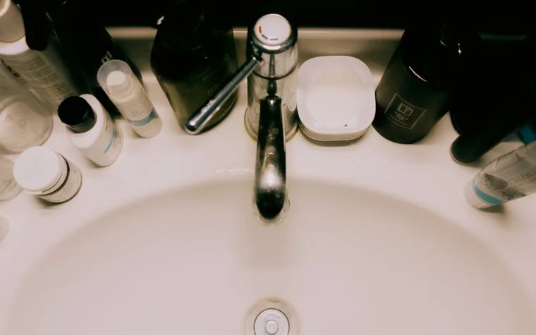 Overhead view of a bathroom sink with a tap, soap dish and bottles of toiletries around it