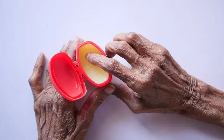 Senior hands scooping balm from a small red tin with the fingertips