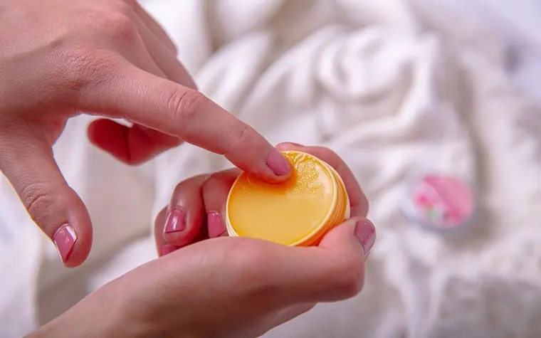 Woman holding a small container of lip balm and applying it to her lips