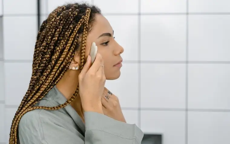 A woman presses a cotton pad to her cheek in a bright bathroom