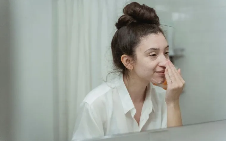 A smiling woman with her hair in a bun touching her nose