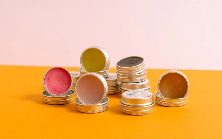 Assorted lip balms in small metal tins on an orange surface