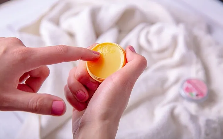Hand applying a yellow balm from a small tin above a white towel