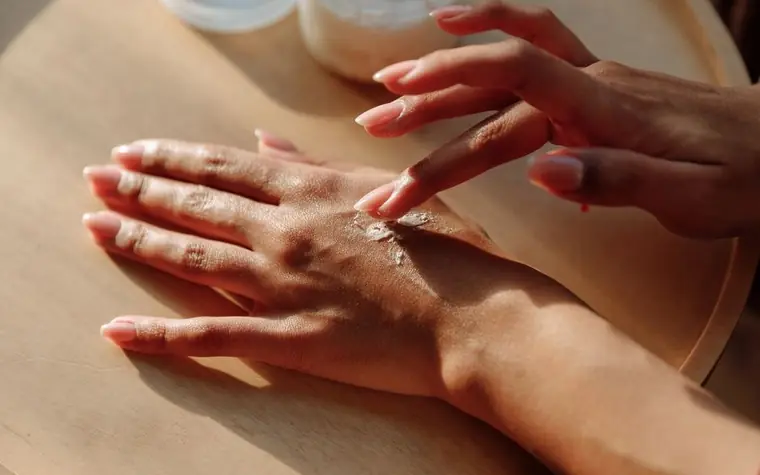 Hands applying a small dab of cream to the back of one hand on a wooden table