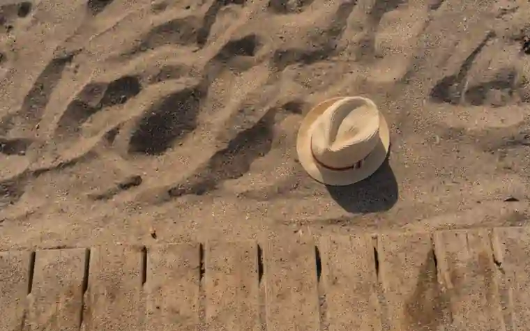 A straw hat lying on sand beside a wooden boardwalk edge in strong sunlight