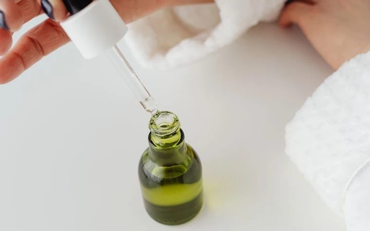 A dropper releasing green serum over a small glass bottle