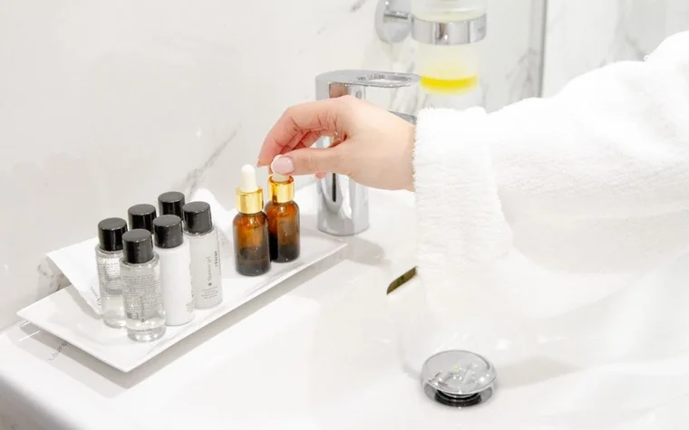 A hand in a white sleeve reaching for small dropper bottles on a white tray