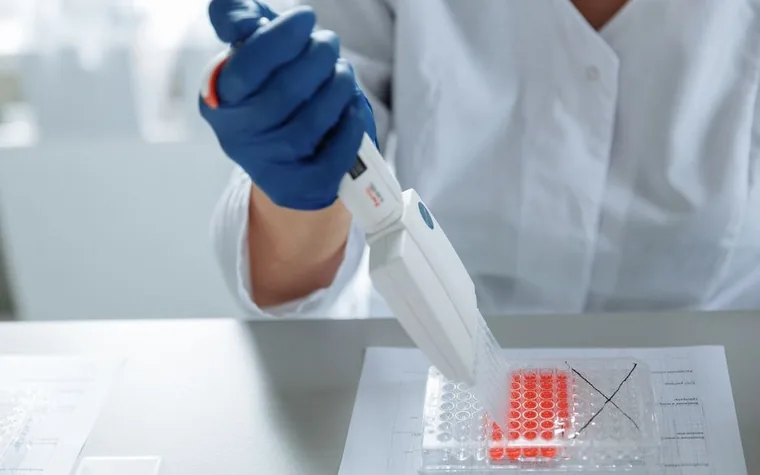 A scientist using a pipette over a sample tray in a laboratory