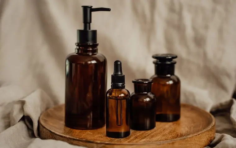 A set of amber glass skincare bottles arranged on a wooden tray