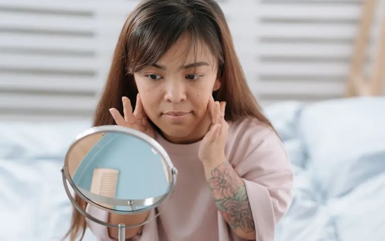 A woman checking her skin in a mirror at home