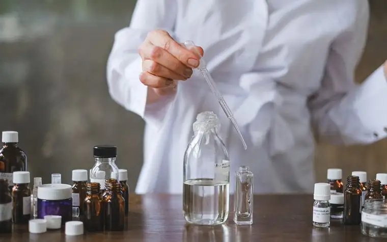 A gloved hand using a dropper to mix liquid among small glass bottles