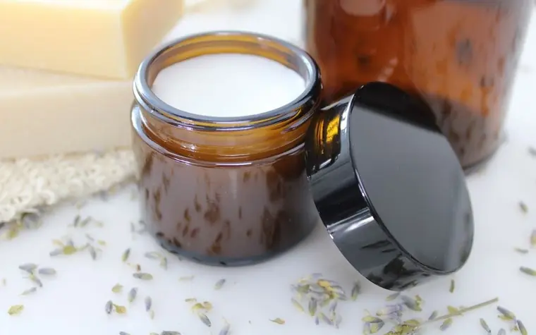 An amber glass cream jar next to a cotton pad and dried lavender