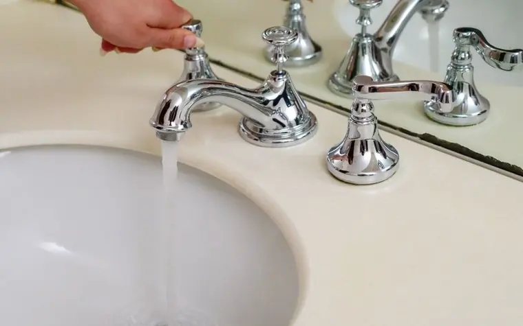 A chrome bathroom faucet running water into a white sink