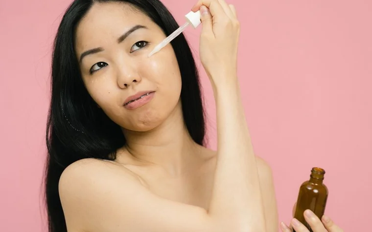 Woman holding a dropper bottle of skincare serum against a pink background