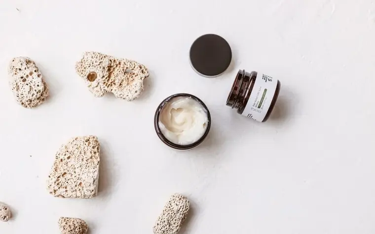 Top view of a skincare cream jar with exfoliating stones on a marble surface