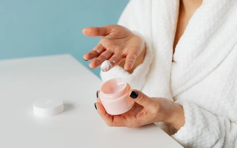 Woman in a white robe holding an open jar of face cream