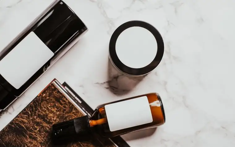 Amber dropper bottle and cream jar with blank labels on a marble surface