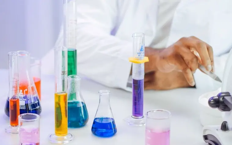 Rows of laboratory beakers and graduated cylinders holding different colored solutions