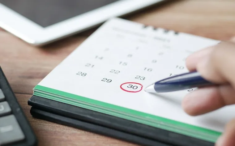 Hand circling the 30th on a paper desk calendar with a blue pen