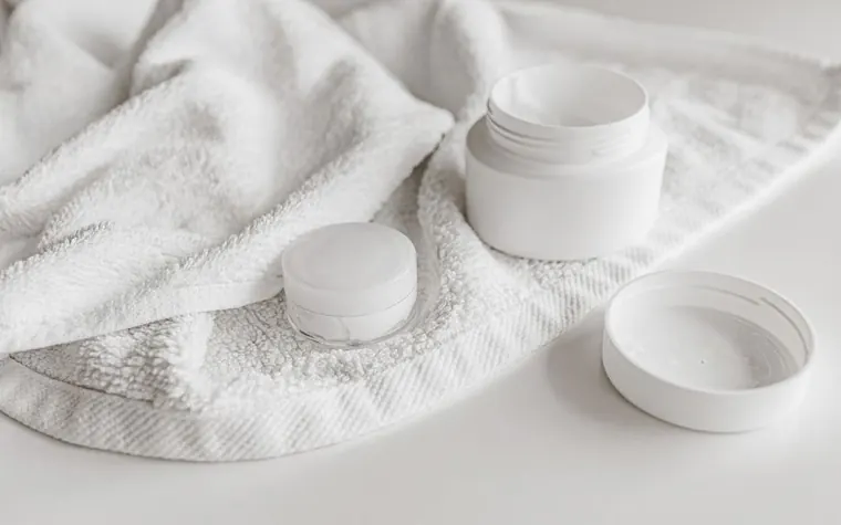 White cream jars and their lids resting on a folded white towel