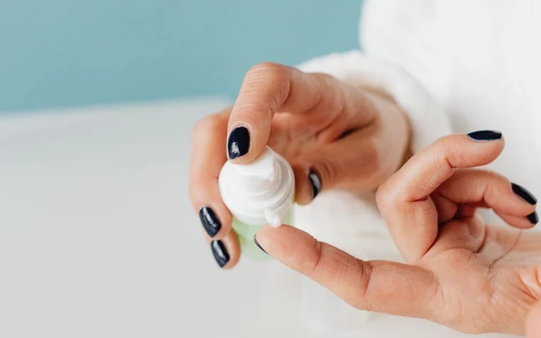 A woman squeezing white cream from a tube onto her fingertips
