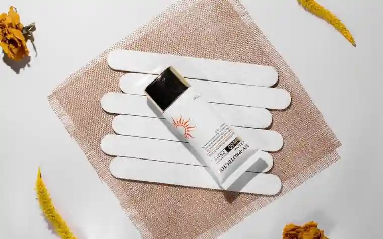 A sunscreen tube on a woven mat with white sticks and dried flowers