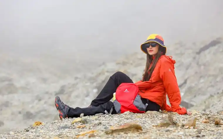 Hiker in a bucket hat and sunglasses resting on rocky terrain in daylight