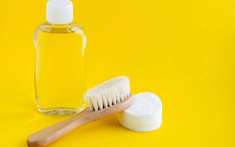Clear glass bottle of cleansing liquid beside a stack of cotton pads on a bright yellow background