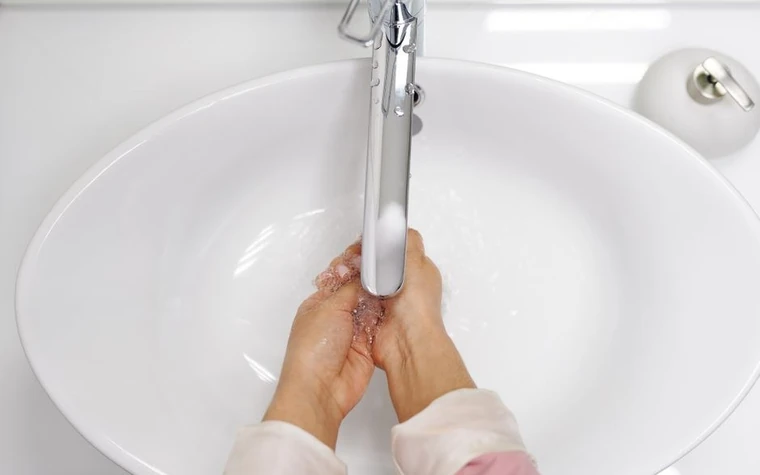 Hands rinsing under a running chrome faucet over a white bathroom sink