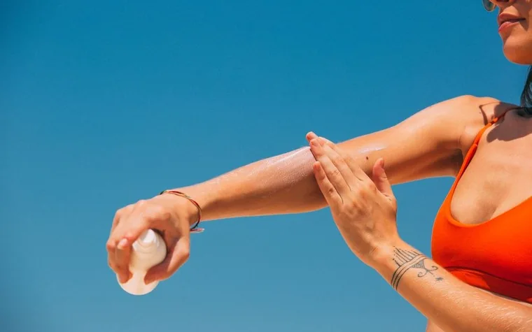 A woman applying sunscreen to her arm outdoors