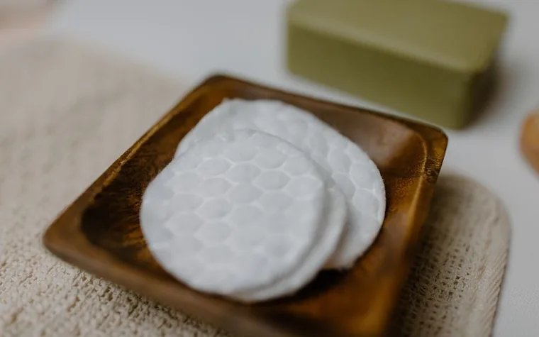 Cotton pads on a wooden tray beside a bar of soap