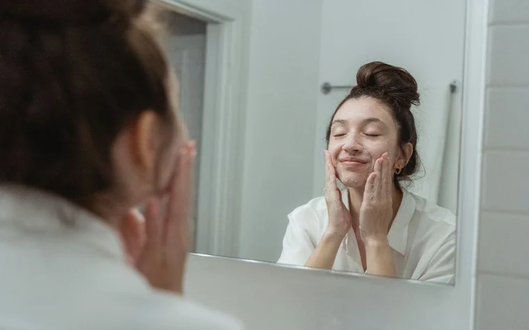A woman washing her face at a bathroom mirror