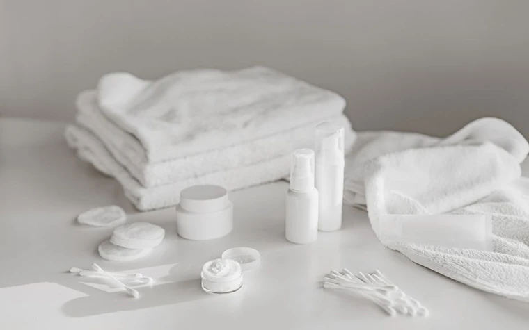 Folded white towels beside white skincare containers