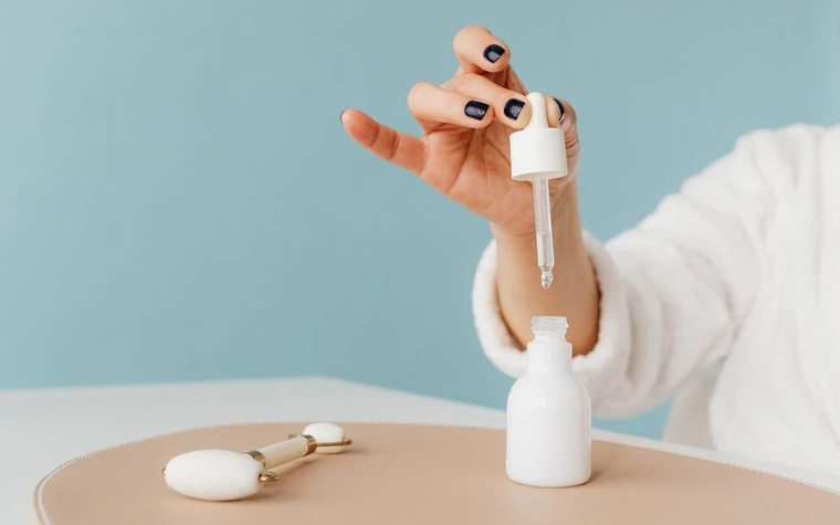 A hand holding a dropper of serum above a bottle
