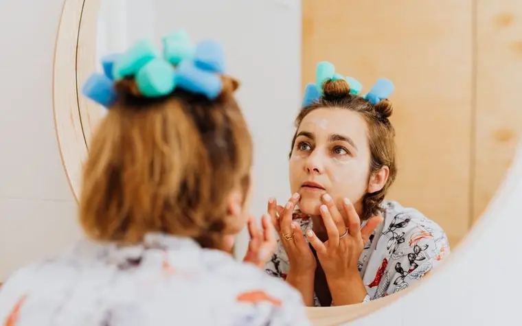 A woman applying cream to her face in front of a mirror