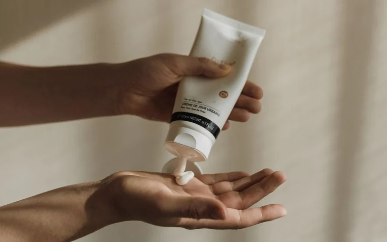 A hand squeezing white sunscreen from a tube onto an open palm