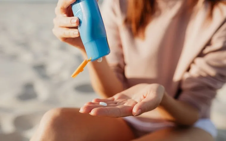 A woman squeezing sunscreen from a tube into her palm outdoors